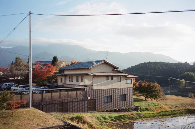 A photo of a house on the side of a small hill, with mountains in the background